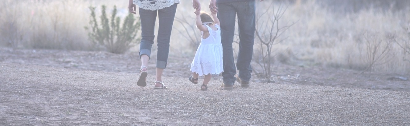 Toddler walking with her parents and holding hands.