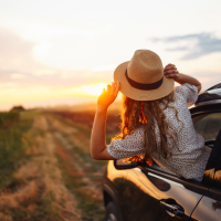 Girl hanging out the car window looking at the road behind her.