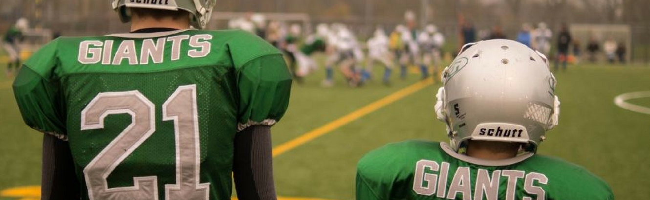 Two football players watching their team on the field.