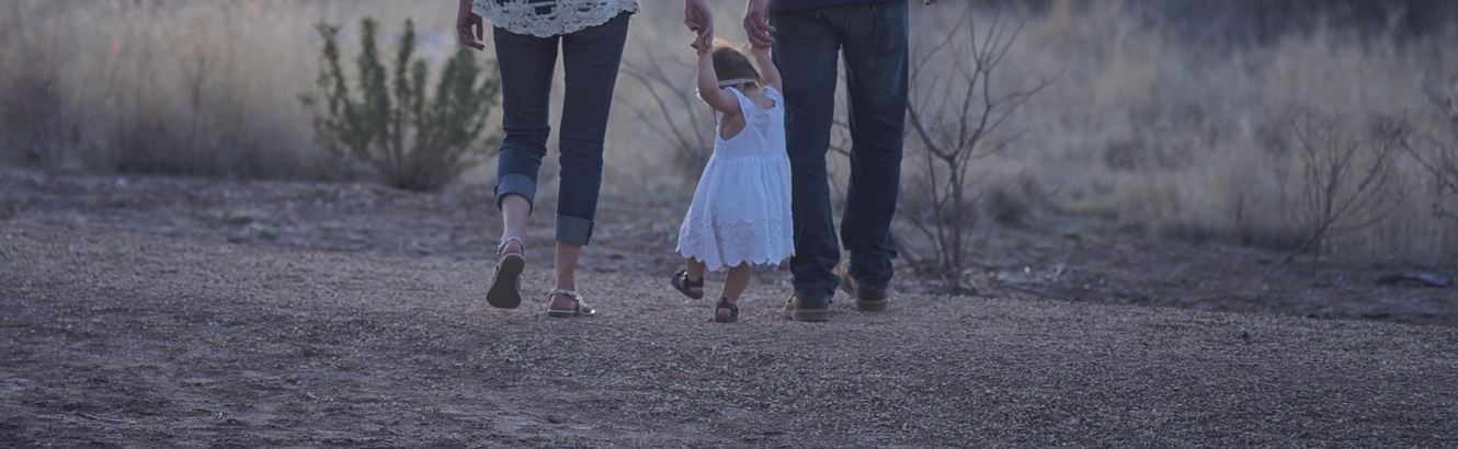 Toddler walking with her parents and holding hands.
