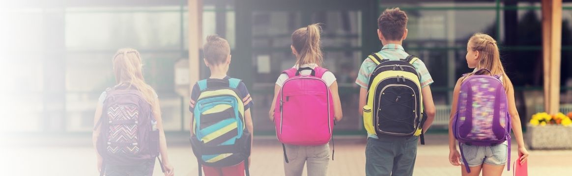 View of 5 school age kids wearing backpacks and walking toward the school.