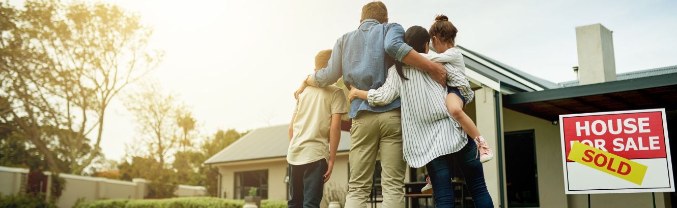 Family hugging in front of new home they bought