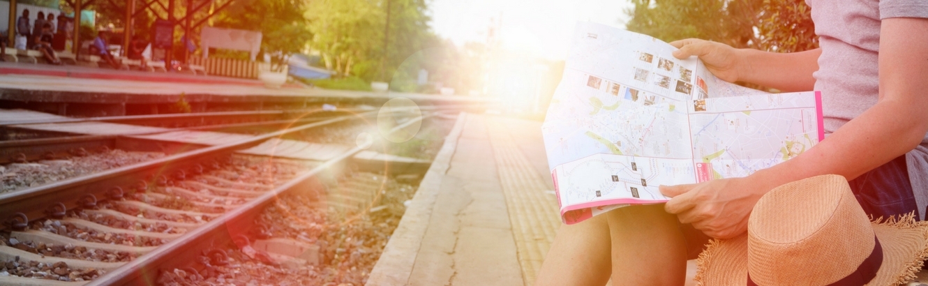 Person reading a map while sitting by train tracks.