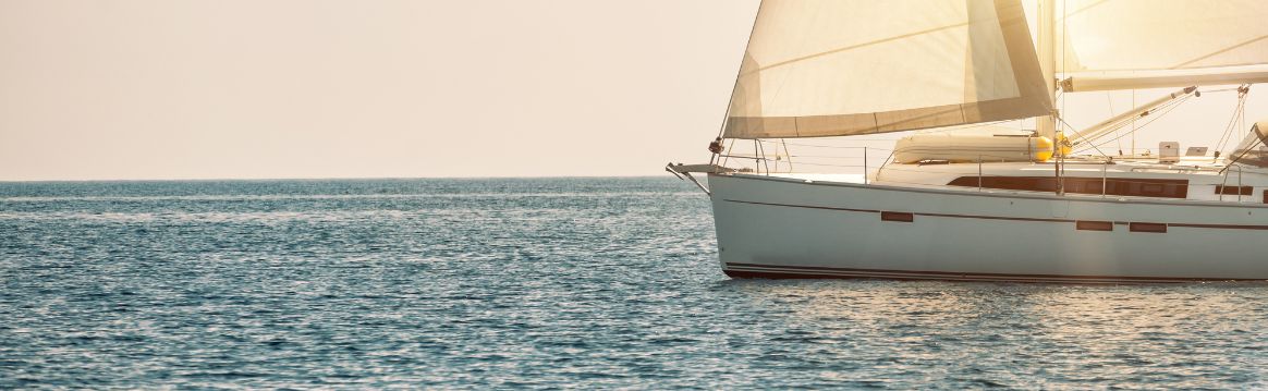 Sailboat in the middle of the ocean with sun shining through sails