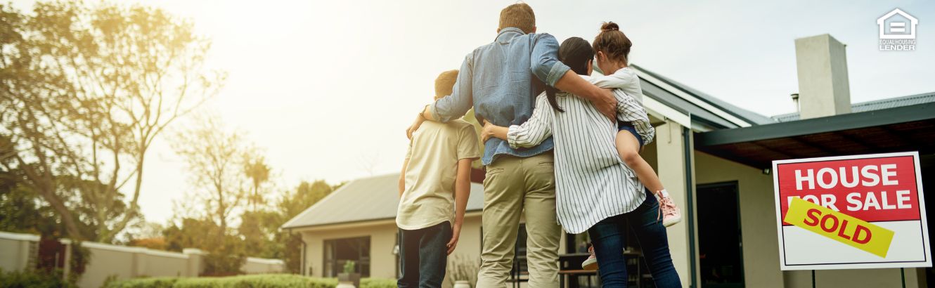 Family hugging in front of new home they bought
